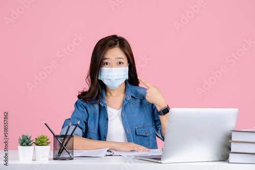 Young asian businesswoman in casual clothes and wearing a mask to prevent covid 19 isolated on pink background studio.