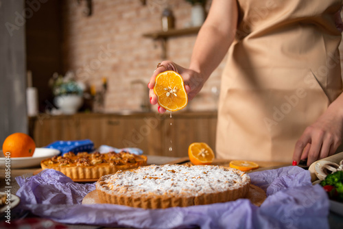 the cook girl squeezes juice from an orange onto a pie