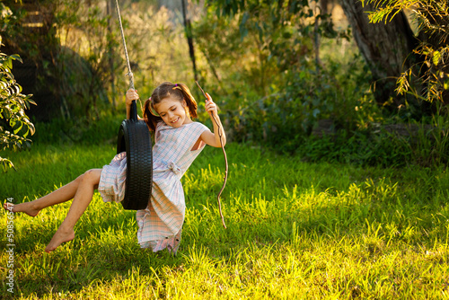 Young country girl playing alone outdoors on tyre swing photo