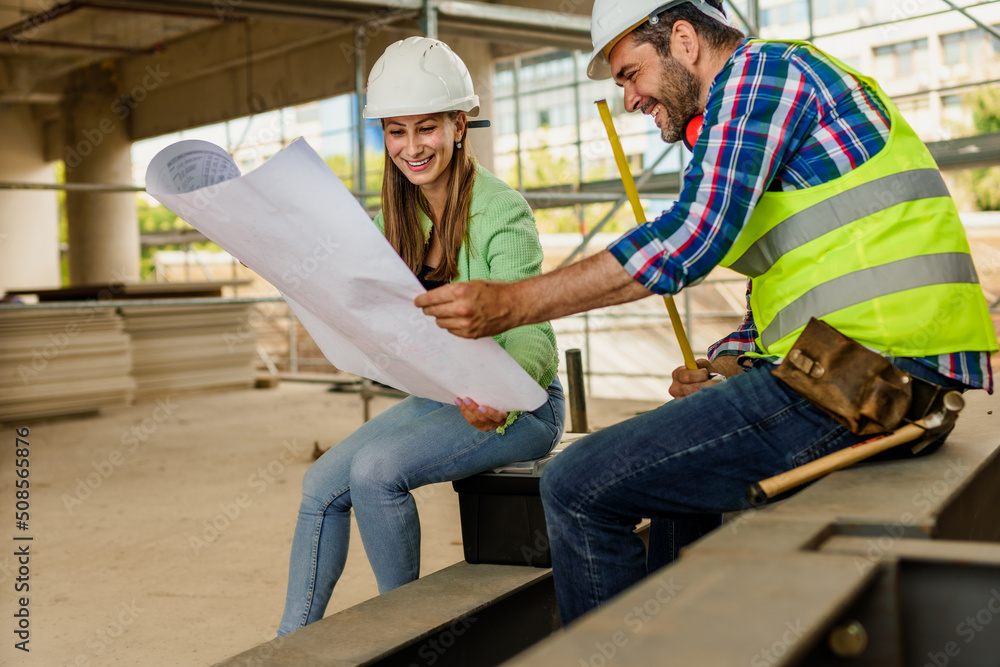Two happy civil engineer and maintenance engineer in protective vests and helmets working on a construction site Two happy civil engineer and maintenance engineer in protective vests and helmets working on a construction site
