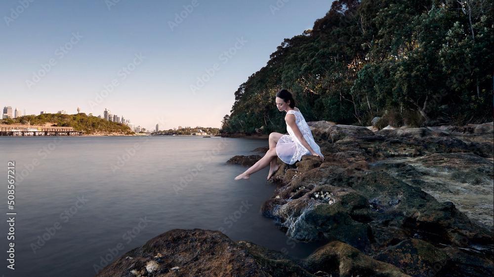 Girl peacefully relaxing by the water's edge in a white dress Girl peacefully relaxing by the water's edge in a white dress