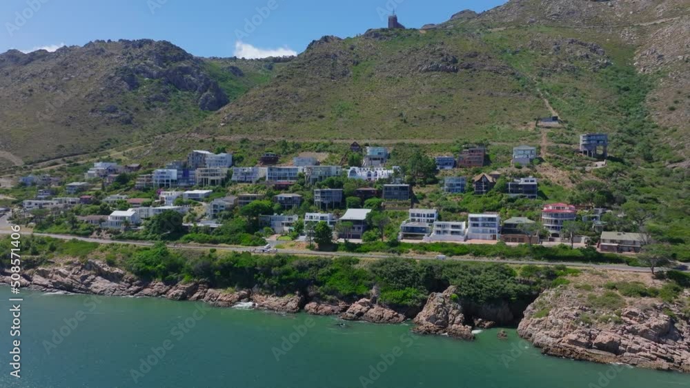 Pan shot of buildings along road leading on sea coast. Tourist destination with mountain ridges in background.