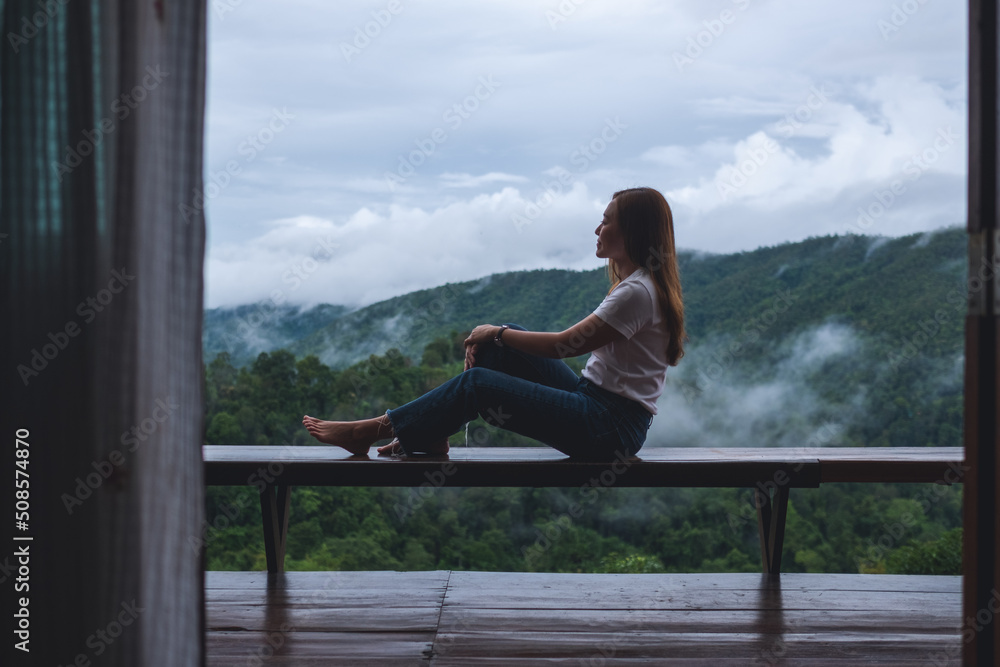 Portrait image of a woman sitting on wooden balcony with a beautiful mountains and nature view on foggy day Portrait image of a woman sitting on wooden balcony with a beautiful mountains and nature view on foggy day
