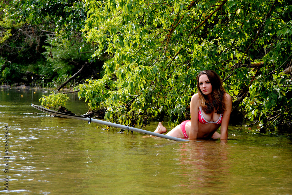 Fototapeta premium Beautiful young Ukrainian woman on the river under a tree in a red swimsuit