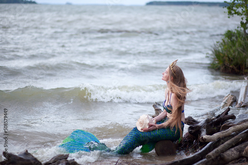 Mermaid story. The little mermaid sits on the seashore. Mermaid at sunset. Mermaid's tail. Mermaid costume. Long hair.
