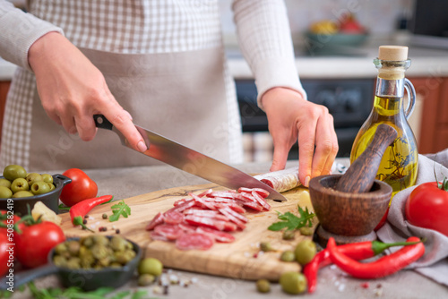 Woman slicing Spanish sausage fuet salami with knife on a domestic kitchen photo