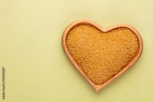 Brown sugar in heart wooden bowl shape on pasttel background.