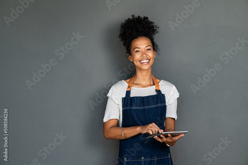 Black happy waitress in apron using digital tablet to take orders