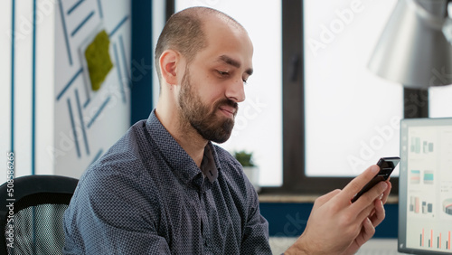 Business man looking at smartphone to browse internet, working with sales statistics to plan marketing growth. Male employee with financial expertise working with mobile phone.