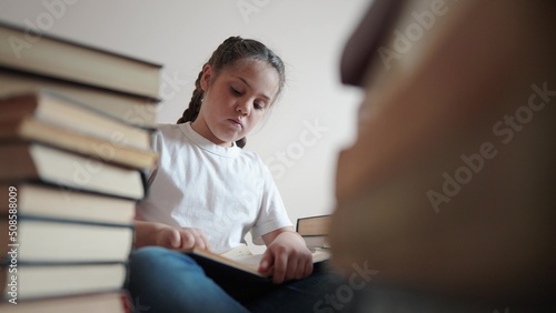 little girl in the library reading a book. education school lifestyle kid science concept. a child sits on the floor stacks of books flips through the pages reads studies. daughter reading a book