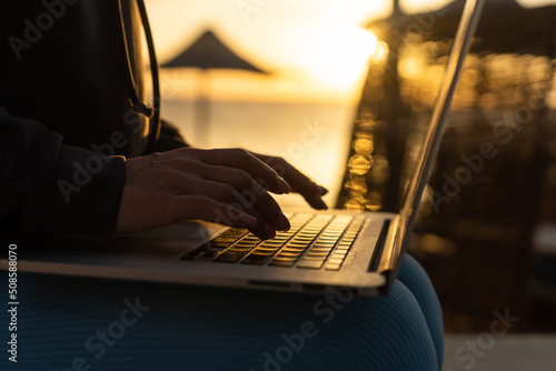 Canvas Print Close-up image of woman sitting on sandy beach and working on laptop, coding or answering e-mails
