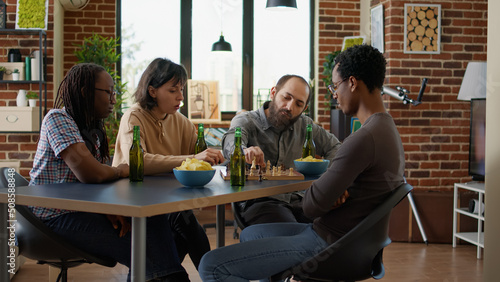 Group of people thinking about next move at chess board game, playing together with alcoholic drinks and snacks. Cheerful friends having fun with modern gaming activity for leisure.