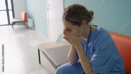 Overworked nurse sitting on bench in hospital corridor photo