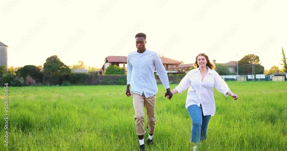 Multi ethnic couple running in meadow holding hands Multi ethnic couple running in meadow holding hands