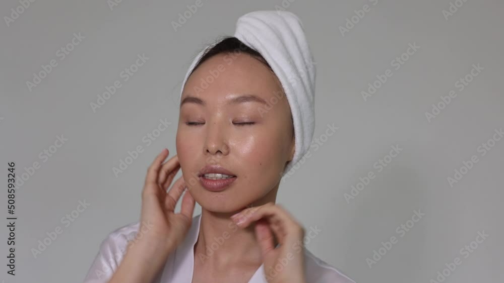 Closeup of asian woman face. Neutral natural pink manicure on nails. Beautiful portrait with towel on head. Woman showing her ideal skin Closeup of asian woman face. Neutral natural pink manicure on nails. Beautiful portrait with towel on head. Woman showing her ideal skin