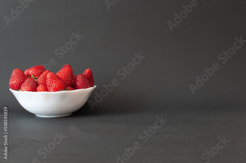 Strawberries, natural and sweet ripe strawberries in white bowl with copy space on right. Isolated on dark background, selective focus.