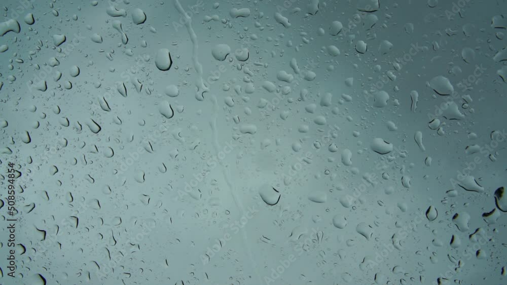 Close-up of water droplets on glass. Large rain drops strike a window pane during a summer shower. 4K.