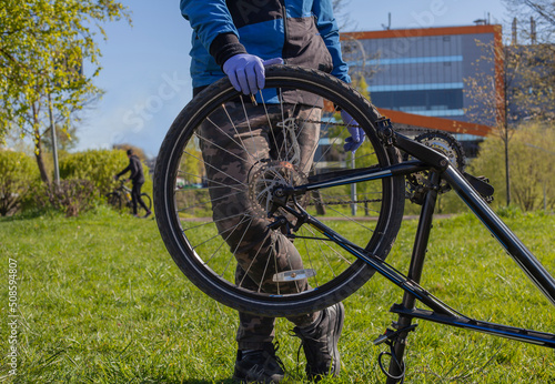 Man reparing bicycle wheel. Cyclist changing tire diy. Looking for bicycle tires leak. Examining bike for issues in park. Back bicycle tire wobbles problem solving. photo