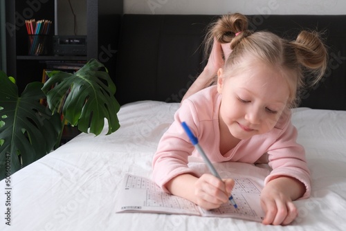 Portrait of a schoolgirl solves children crosswords on the bed. Logic games at home. Children solves crossword photo