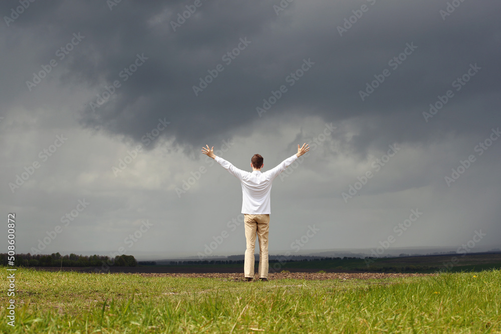 Man in white shirt with raised hands and grey sky with stormy clouds. Photo was taken 15 May 2022 year, MSK time in Russia. Man in white shirt with raised hands and grey sky with stormy clouds. Photo was taken 15 May 2022 year, MSK time in Russia.