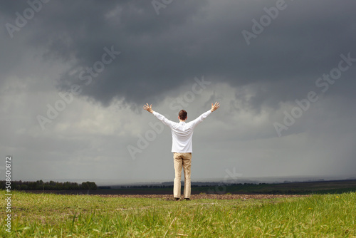 Man in white shirt with raised hands and grey sky with stormy clouds. Photo was taken 15 May 2022 year, MSK time in Russia.