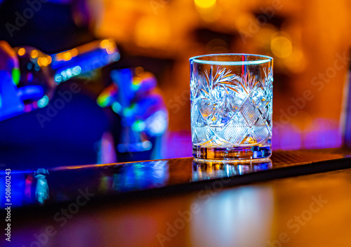 woman bartender hand pours alcohol from bottle in glass with ice in nightclub