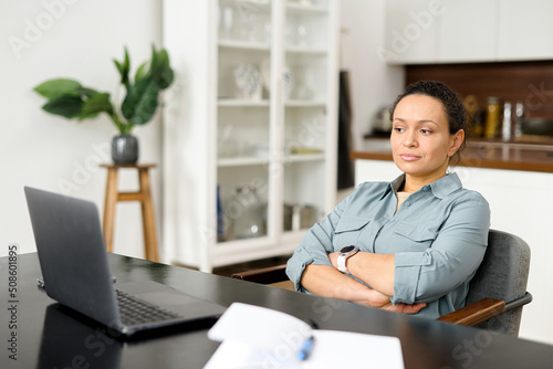 Pensive young woman does not have inspiration for work, feels lack of sleep and fatigue. Bored female office employee sits at the desk in front of a laptop in the office, looks away and feels sad