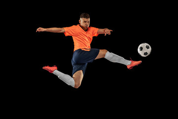 Dynamic portrait of professional male football soccer player in motion isolated on dark background. Concept of sport, goals, competition, hobby, achievements