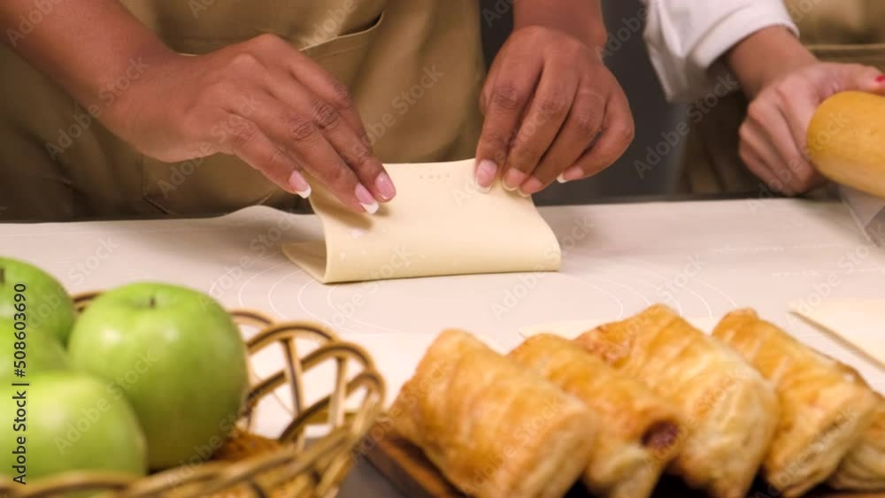 Close-up at the hand of chef in cook uniform with apron, cooking class students roll and stuff ingredients in pastry dough for bakery foods, prepare fruit pies in restaurant stainless steel kitchen. Close-up at the hand of chef in cook uniform with apron, cooking class students roll and stuff ingredients in pastry dough for bakery foods, prepare fruit pies in restaurant stainless steel kitchen.