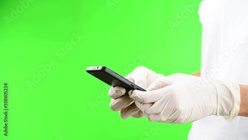 Woman texting with her smartphone with protective white latex gloves against large green background and with large copy space