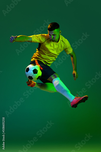 Studio shot of young professional male football soccer player in motion isolated on green background in neon. Concept of sport, goals, competition, hobby, achievements © master1305