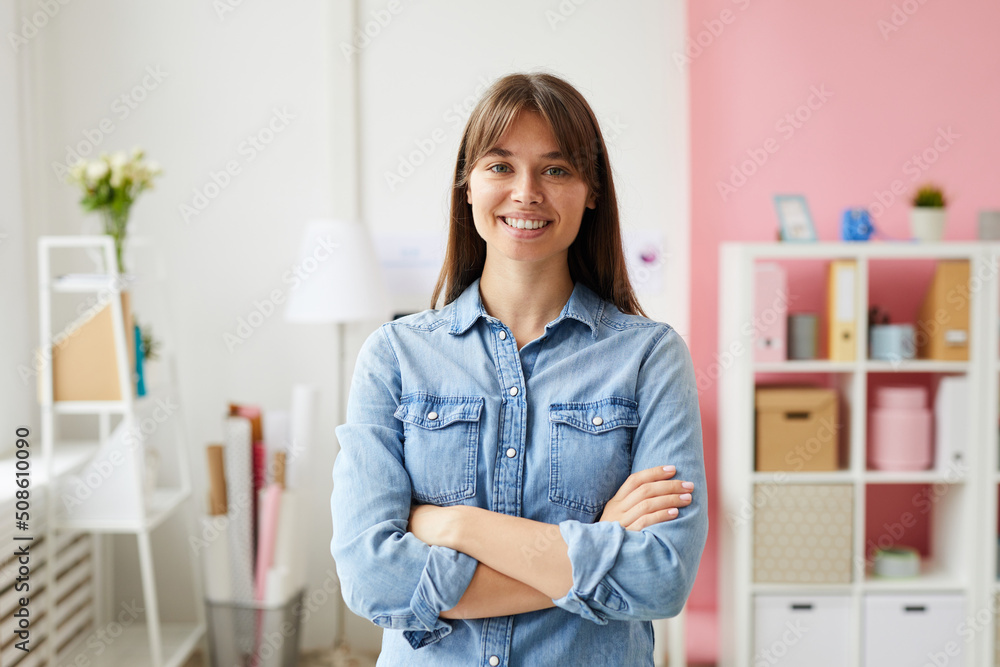Portrait of smiling confident young lady with brown hair wearing denim shirt standing in office with pink interior Portrait of smiling confident young lady with brown hair wearing denim shirt standing in office with pink interior
