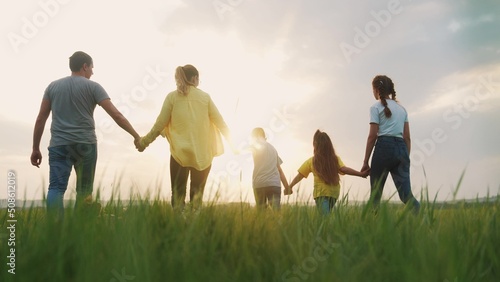 people in the park. happy family a silhouette walk in field. mom dad and daughters, son walk holding hands in park. happy family kid dream concept. parents and children walking back fun silhouette