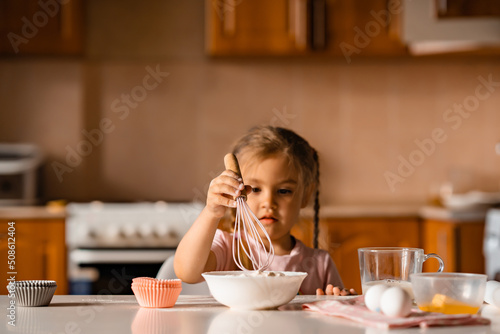 Cute little blonde girl cooking dough in kitchen at home