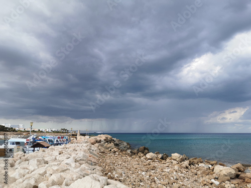 Large rocks on the shores of the Mediterranean Sea, dramatic skies and rain over the largest sailing yacht in the world, an eight-deck motorsailer. photo