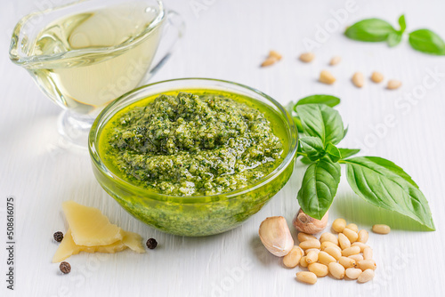 Italian homemade herbal pesto sauce made of blended parmesan cheese, green basil leaves, pine nuts, garlic, black pepper and olive oil served in glass bowl on white wooden background used on pasta