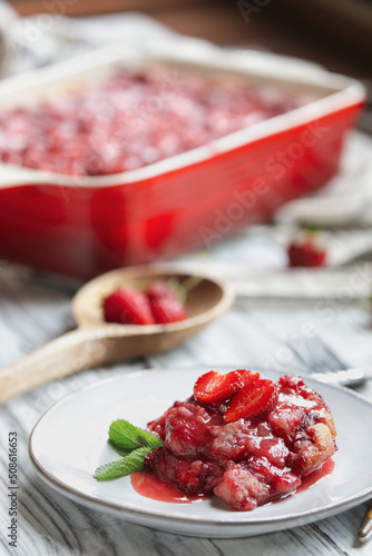 Sweet homemade strawberry cobbler or Sonker baked in a red ceramic pan over a rustic white wood table. Extreme selective focus with blurred background.