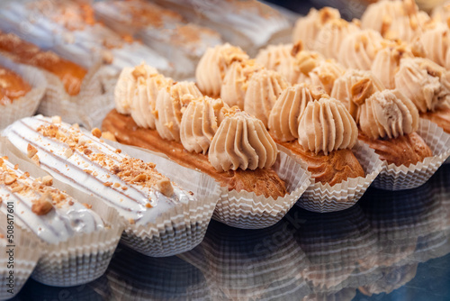 Eclairs on the shelf of a pastry shop or cafe. Tasty french sweets on window shop, delicious pastries for coffee. Cakes in pastry shop, variety of desserts with creamy topping on display in bakery