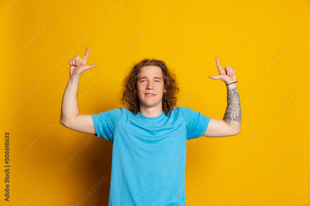 Young emotional man with long curly hair posing isolated on yellow background. Human emotions, facial expression concept. Trendy colors