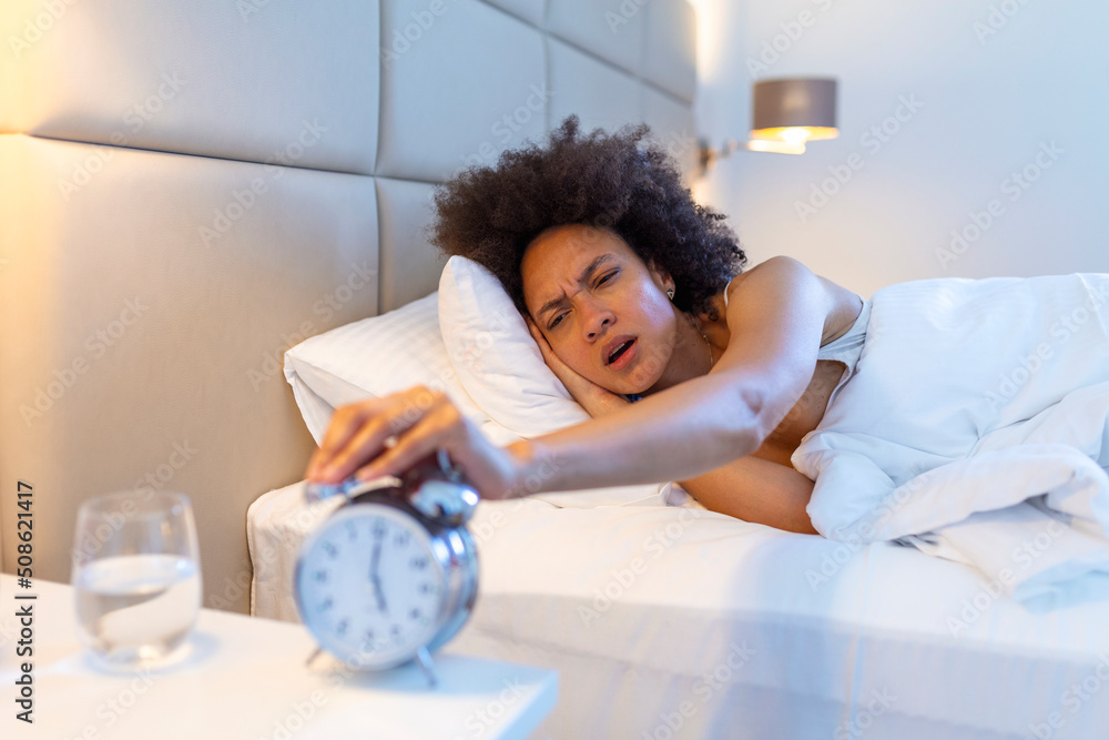 Wake up of an asleep girl stopping alarm clock on the bed in the morning. woman sleeping and