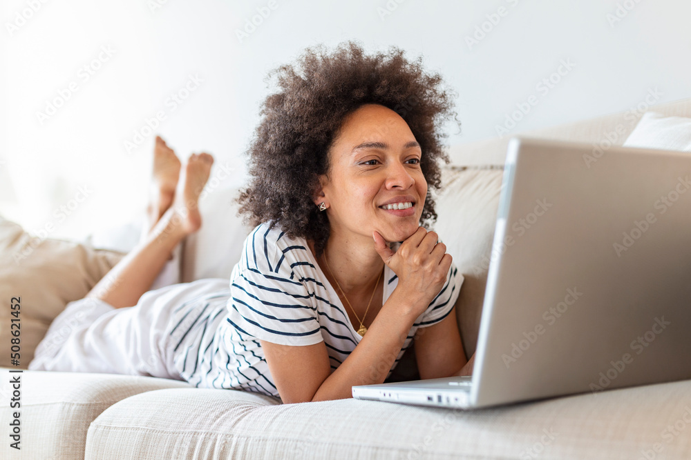 Young beautiful woman with curly hair working on laptop computer while sitting on the sofa at home Young beautiful woman with curly hair working on laptop computer while sitting on the sofa at home