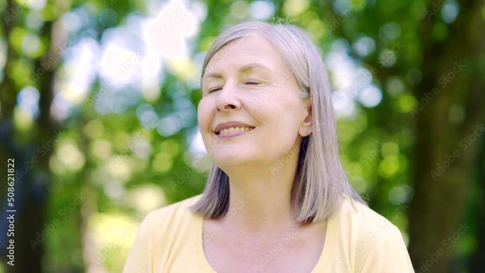 Close up portrait senior retiree woman standing in nature between forest trees relaxes, breathes fresh air closing eyes. Mature female enjoys a life of peace calm, quiet in the park. Outdoor Happiness Close up portrait senior retiree woman standing in nature between forest trees relaxes, breathes fresh air closing eyes. Mature female enjoys a life of peace calm, quiet in the park. Outdoor Happiness