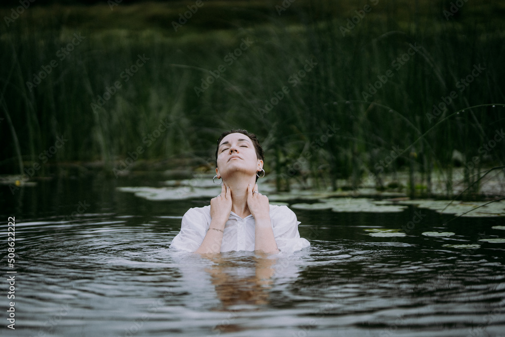 A young woman with a short haircut swims in a forest lake. Portrait A young woman with a short haircut swims in a forest lake. Portrait
