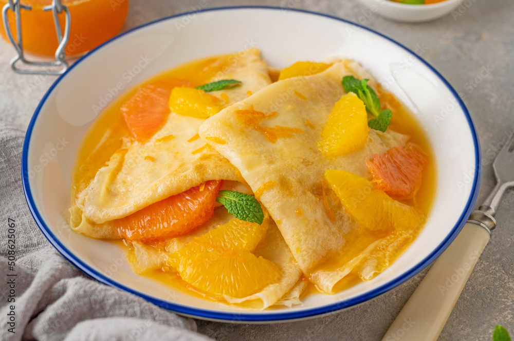 Delicious crepes suzette with orange syrup and slices fruits on a plate on a gray concrete background, top view Delicious crepes suzette with orange syrup and slices fruits on a plate on a gray concrete background, top view