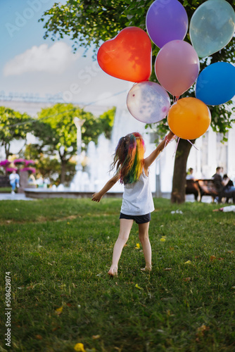 cute little caucasian girl with colourful dyed hair walking barefoot with baloons