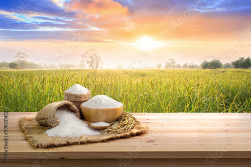 Foto Asian uncooked white rice with the sunset rice field background and burlap sack on wooden table
