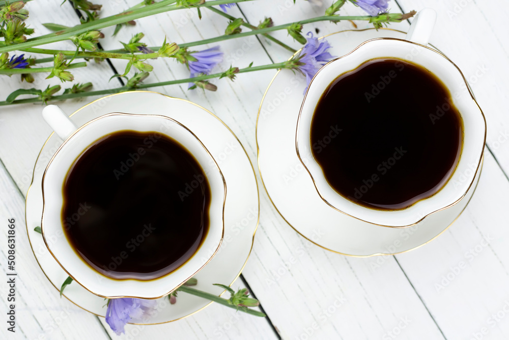 Two cups on saucers with a drink made of chicory root on a white wooden background close-up. A useful substitute for coffee. Two cups on saucers with a drink made of chicory root on a white wooden background close-up. A useful substitute for coffee.