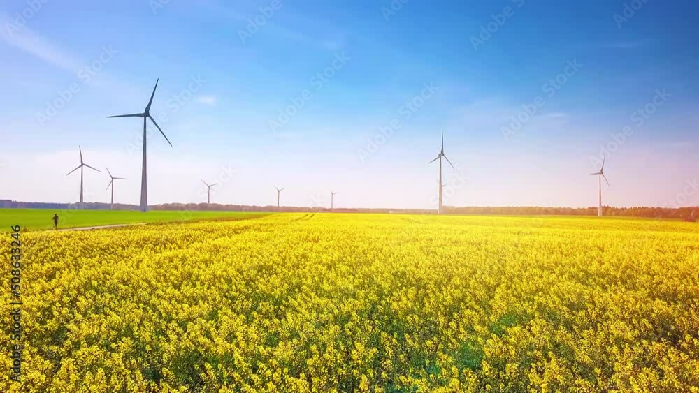 Woman running in rapeseed field, 4K. Nature background with wind turbines Woman running in rapeseed field, 4K. Nature background with wind turbines