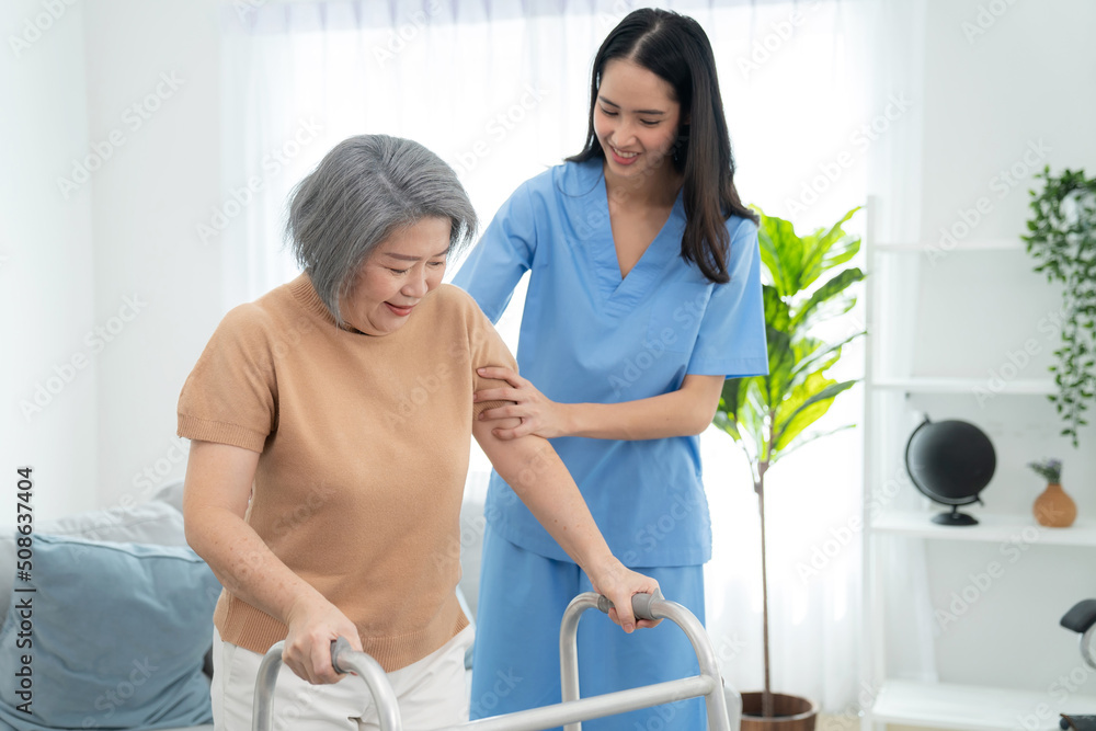 Fototapeta premium Elderly woman stand and walking with caregiver nurse at home. Attractive caregiver help to support arm. Senior patient do physical therapy and exercise muscle. Healthcare and lifestyle concept