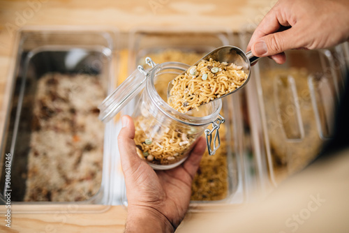 Woman putting dry pasta in glass jar in shop